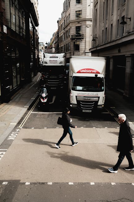 A mid-sized white and blue van belonging to Clapham Removals is parked on a city street in front of a row of multi-storey buildings with varied architectural styles, including brick and ornate facades